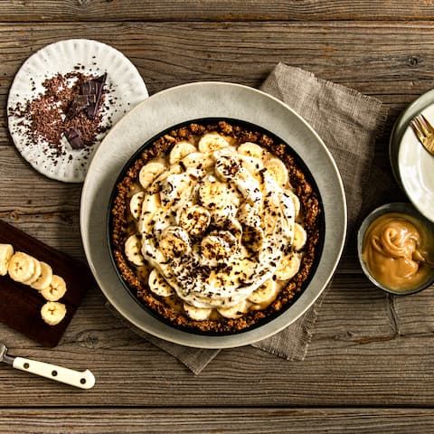 Selbstgemachter Butterkeks-Boden, aus Kondensmilch entstandenes Toffee, Bananenscheiben und eine Sahne-Crème-fraîche-Creme werden nur noch durch und mit Ahornsirup und Schokoladenraspeln getoppt.