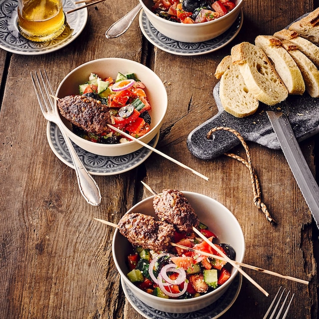 Cevapcici mit griechischem Salat und Weißbrot angerichtet