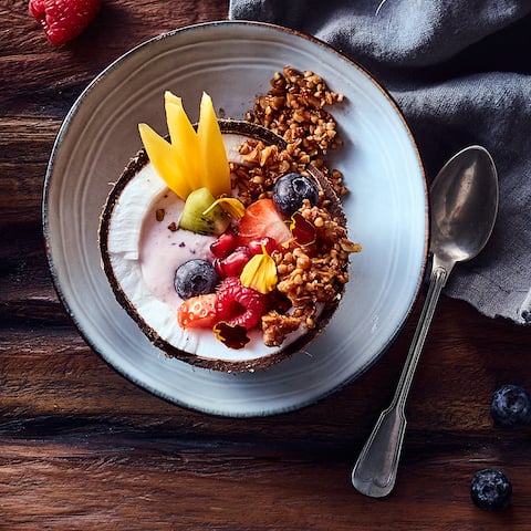 Fruchtige Frühstücks Bowl mit knusprigem Buchweizen-Granola, angerichtet in Kokosnusshälften.