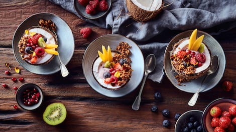 Fruchtige Frühstücks Bowl mit knusprigem Buchweizen-Granola, angerichtet in Kokosnusshälften.