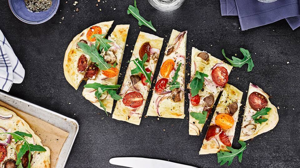 Flammkuchen einmal anders: Als vegetarische Variante präsentieren wir einen Flammkuchen mit Champignons, Zwiebeln, Tomaten und Ziegenfrischkäse. 