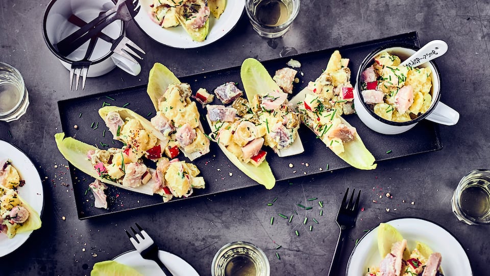 Kartoffelsalat mit Matjes, Gurke und Apfel, im Chicoreeblatt serviert.