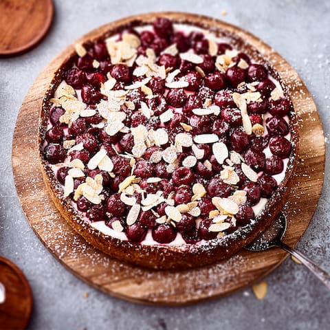Köstlicher und erfrischender Kuchen mit einer Joghurtcreme bilden die ideale Unterlage für süße Kirschen und Mandelblättchen.