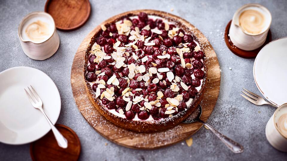 Köstlicher und erfrischender Kuchen mit einer Joghurtcreme bilden die ideale Unterlage für süße Kirschen und Mandelblättchen.