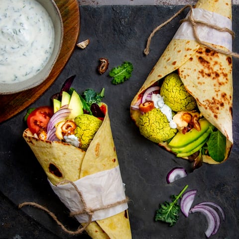Einen orientalischen Touch bekommt unser Rezept für Falafel Wraps durch die Füllung mit Ajvar und Hummus und den leckeren Koriander-Minz-Joghurt.