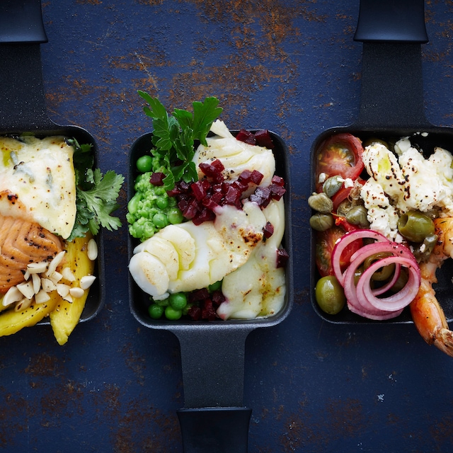 Exotische Raclette-Pfännchen mit viel frischem Fisch und Scampis: Wir servieren Lachs, Kabeljau und Scampi und toppen das Ganze mit vielerlei Käse und Mangospalten. 