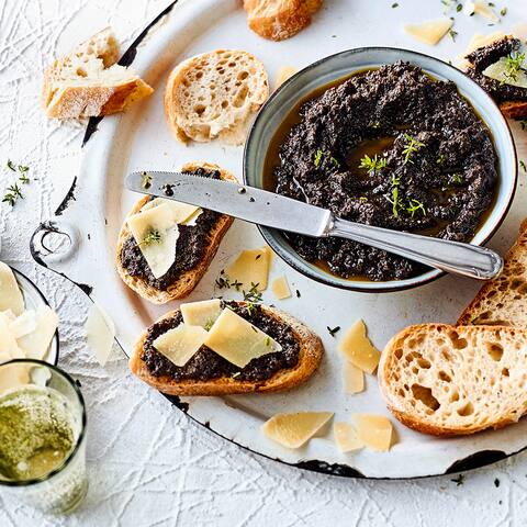 Eine Paste aus schwarzen Oliven, Knoblauch, Sardellen und Olivenöl ist ein würziger Brotaufstrich für Baguette. Garnieren Sie das Ganze noch mit Parmesan und Thymianblättchen!