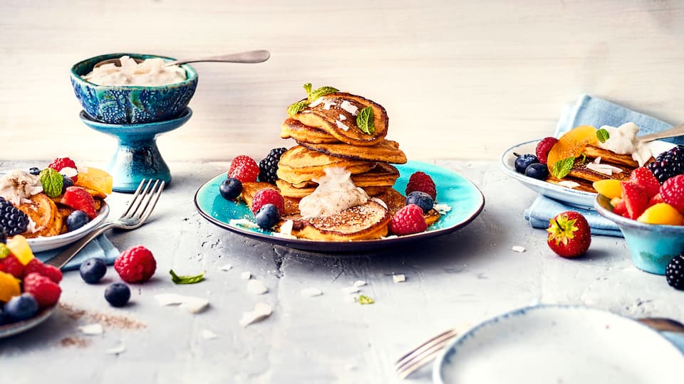 Pfannkuchen einmal anders: Probieren Sie unser Rezept für Süßkartoffel-Pancakes mit Dinkelmehl, frischen Beeren und Kokoschips aus – fruchtig und exotisch!