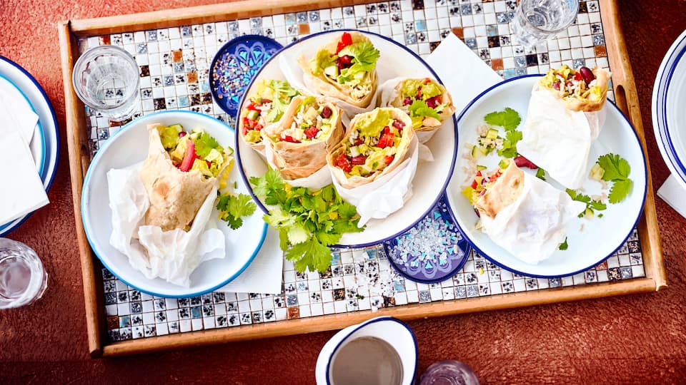 Selbst gemachte Tortillas, gefüllt mit frischem Gemüse, Guacamole, Bohnen und Reis. Ein besonderer Genuss. Probieren Sie unsere veganen mexikanischen Wraps.