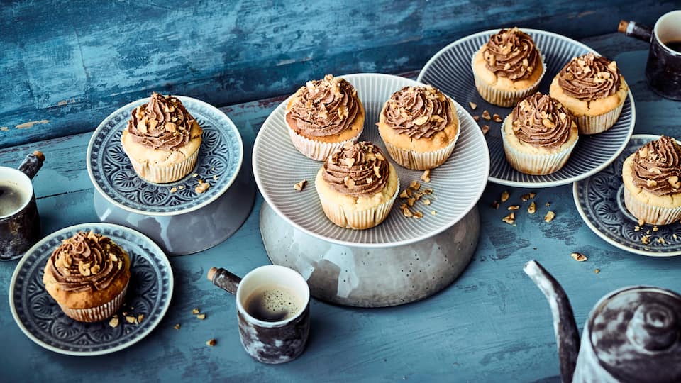 Kleine Küchlein mit Vanille-Soja-Joghurt und Walnüssen, mit einem Schokocreme-Frosting garniert.