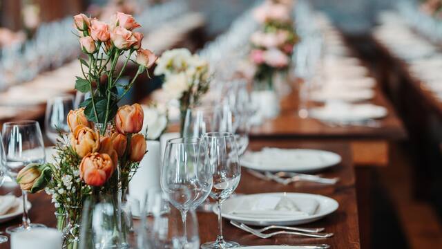 Tischgedeck mit Blumen auf langer Tafel.