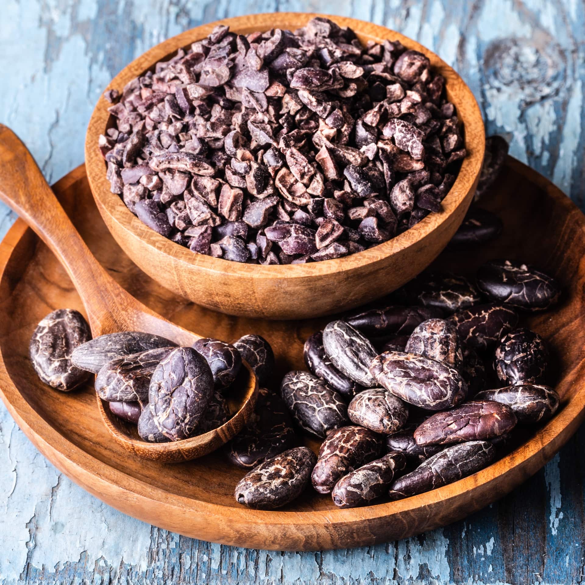 Kakaonibs in Holzschale mit Kakaobohnen und Löffel