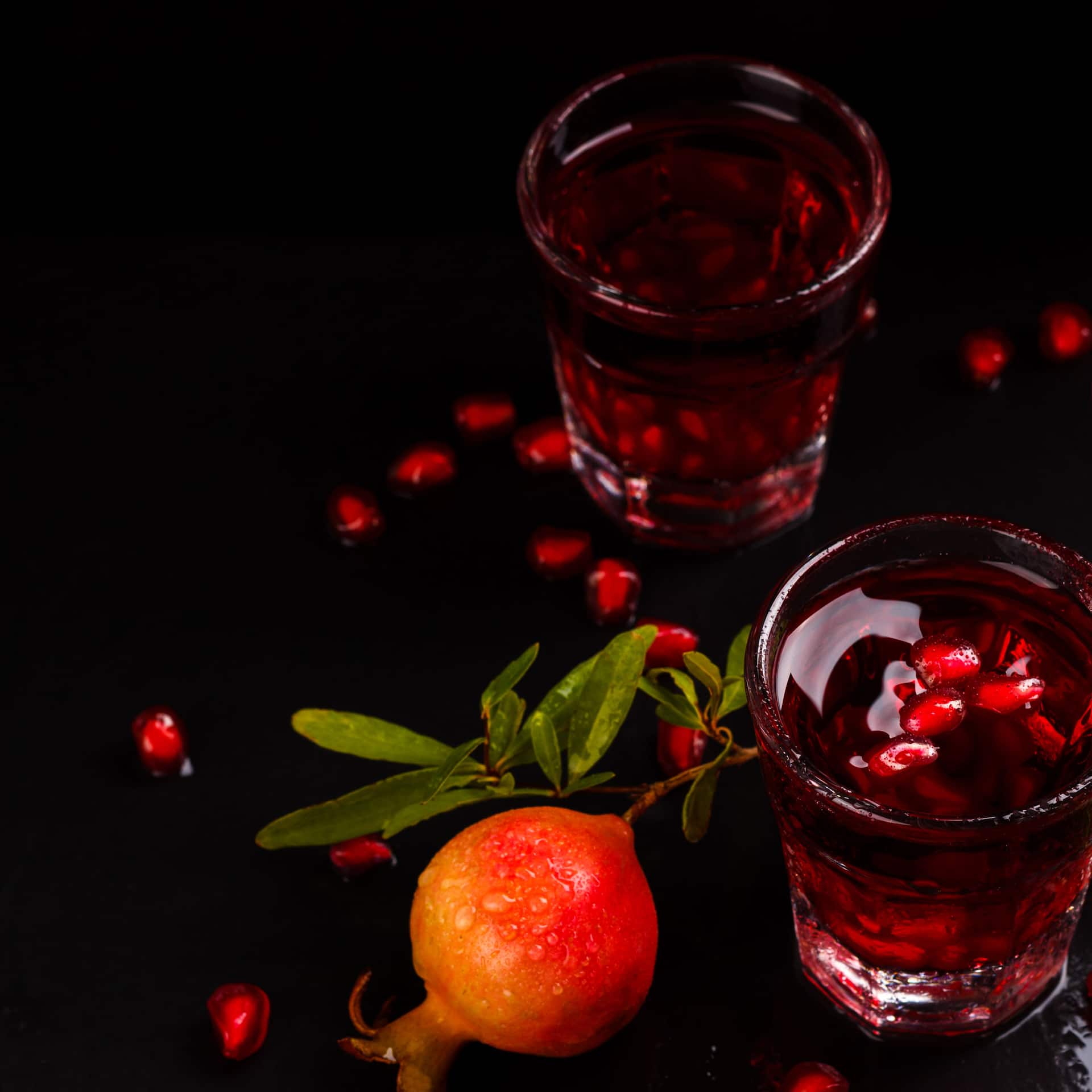 Grenadine im Glas neben Granatapfel auf dunklem Untergrund.