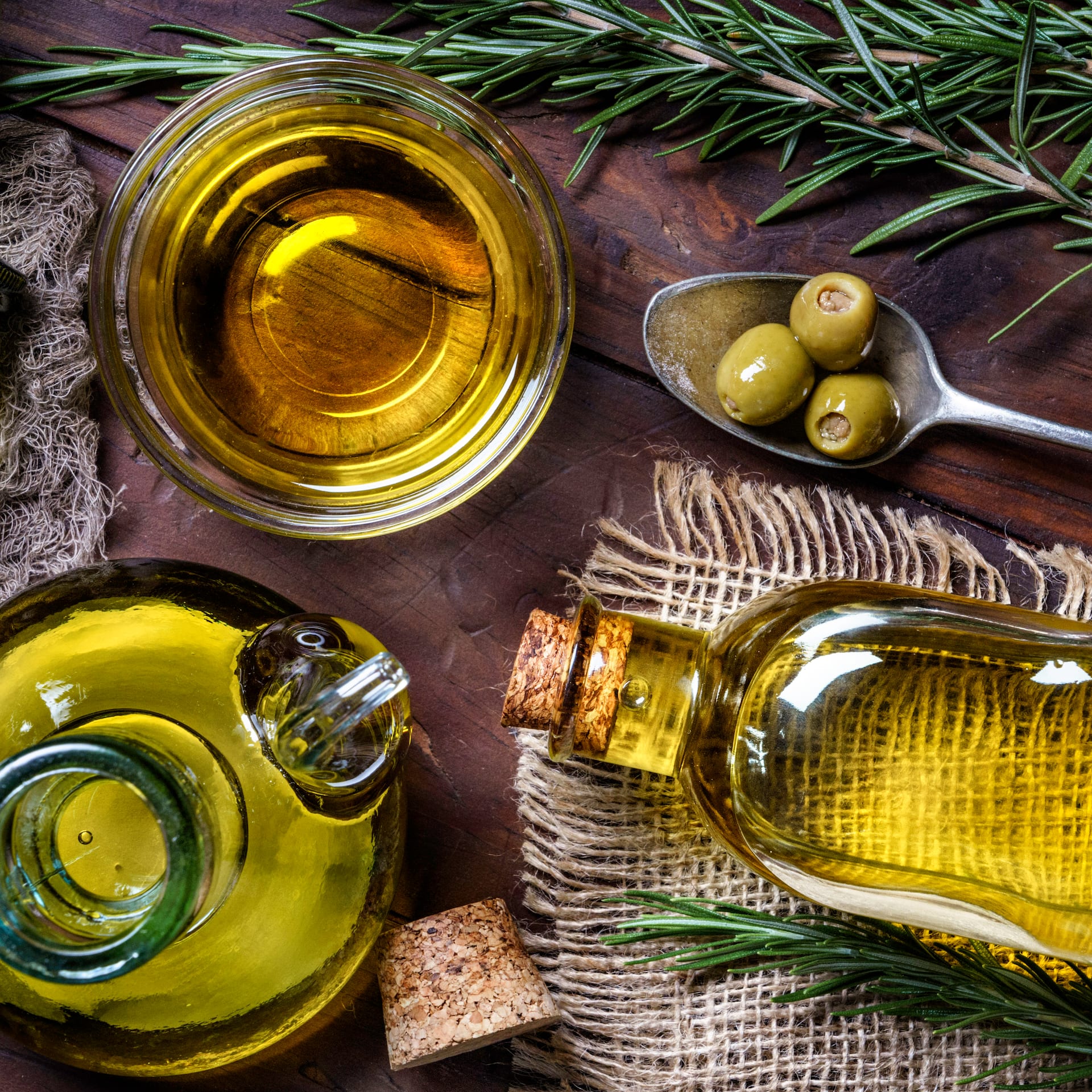 Eine Flasche Olivenöl neben Oliven auf Holzuntergrund