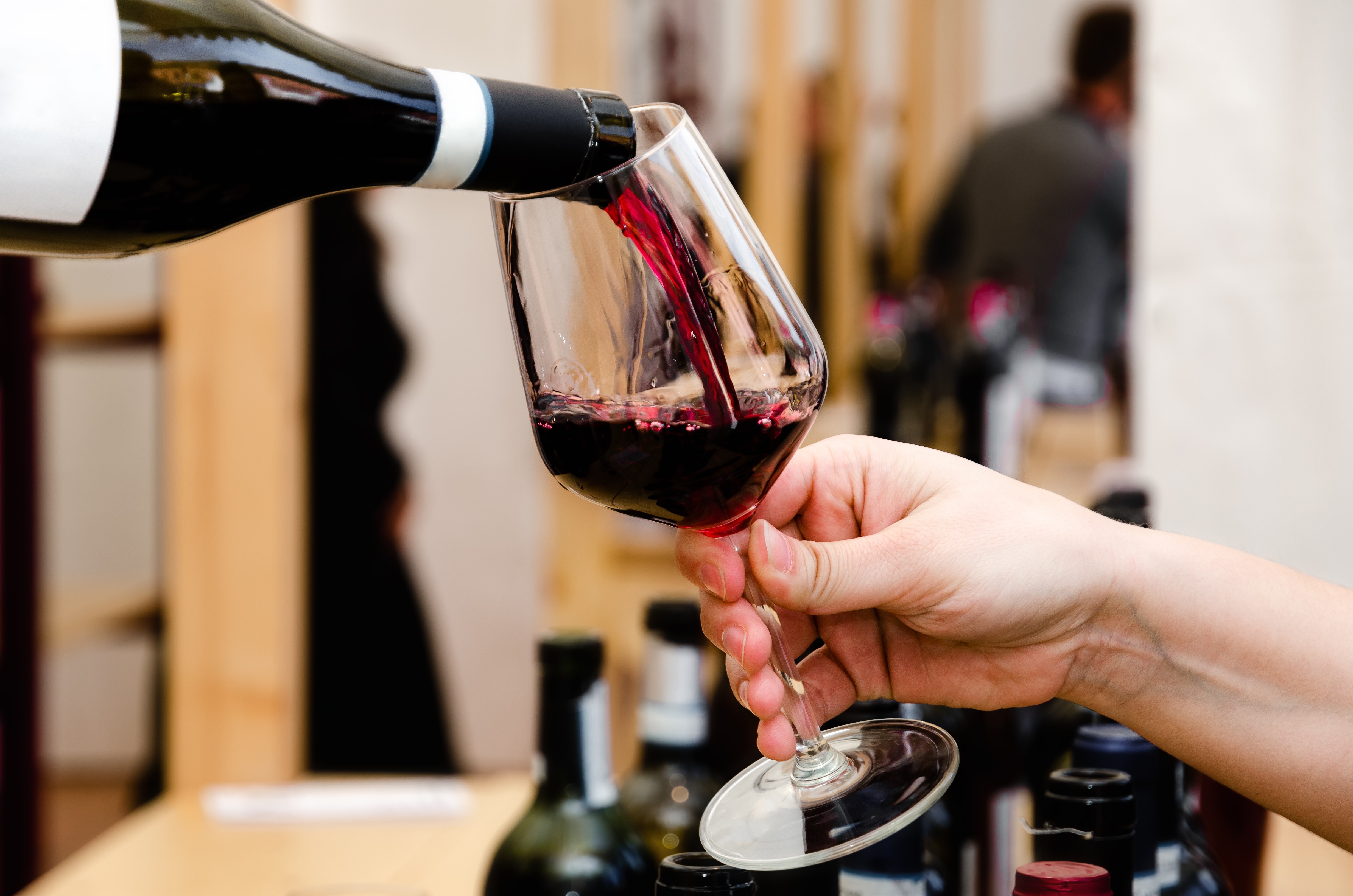 Barolo-Wein wird aus einer Flasche in ein Weinglas eingeschenkt, während mehrere Weinflaschen im Hintergrund stehen.