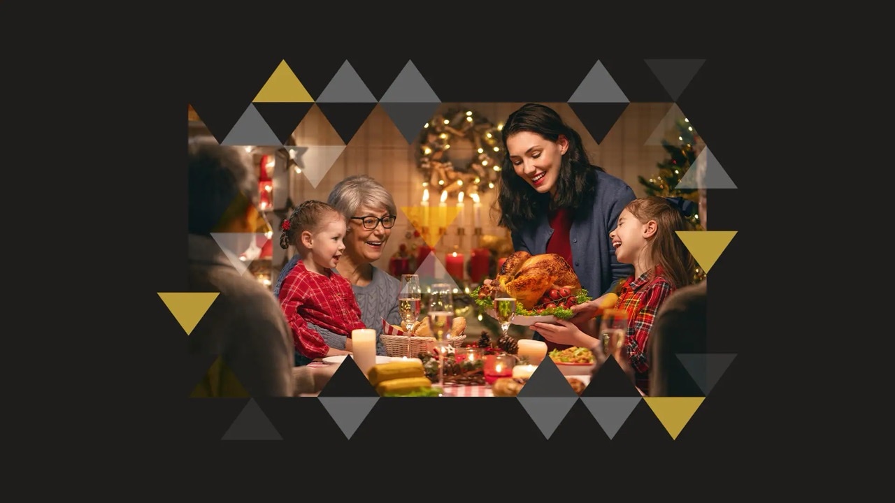 Festlich gedeckter Tisch mit Personen aus drei Generationen. Im Hintergrund sind Kerzen und ein Adventskranz.