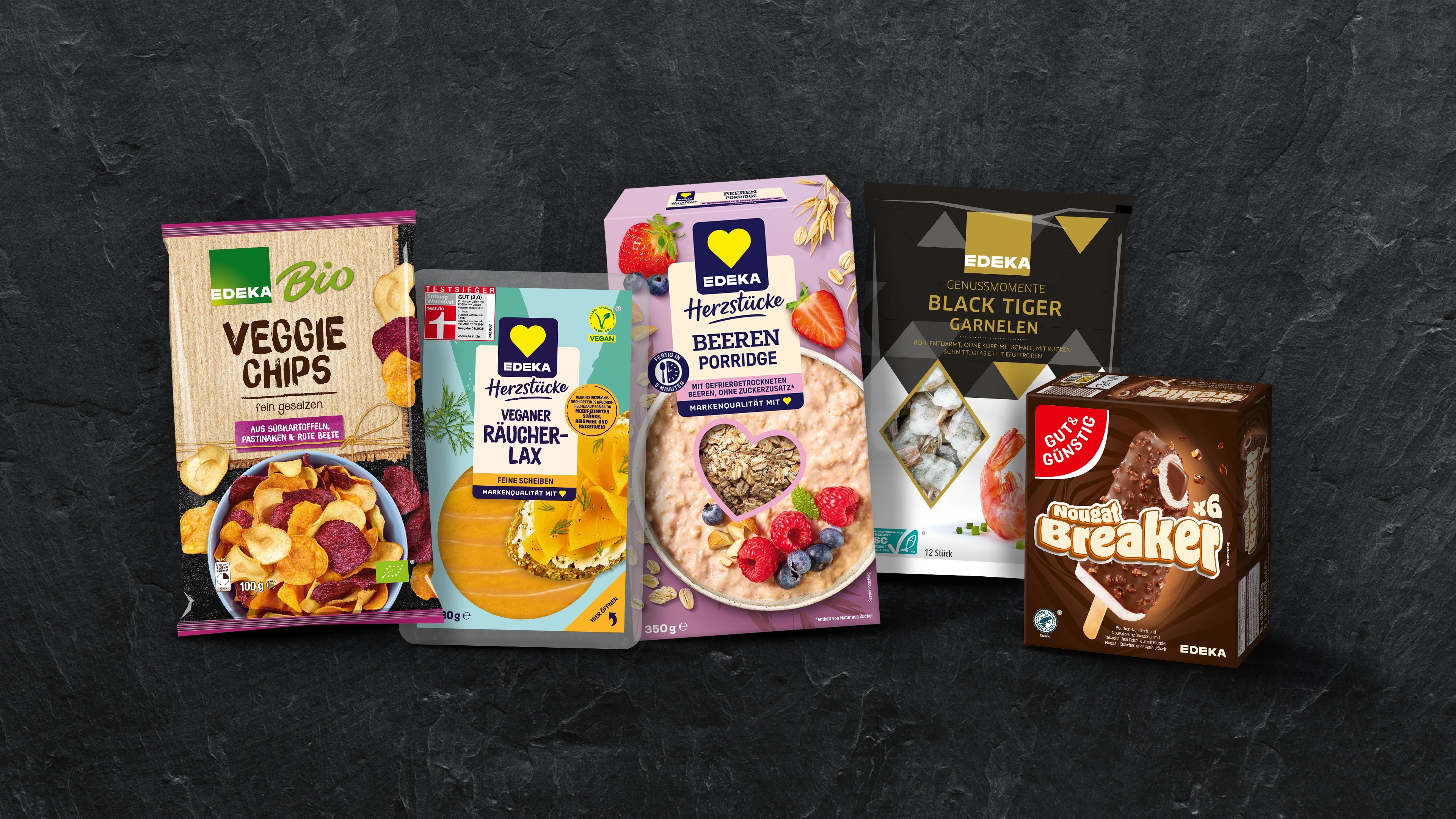 Fünf Produkte vor dunklem Steinuntergrund: EDEKA Bio Veggie Chips, EDEKA Herzstücke Veganer Räucherlax, EDEKA Herzstücke Haferhimmel Porridge Beeren, EDEKA Genussmomente Black Tiger Garnelen und GUT&GÜNSTIG Nougat Breaker.