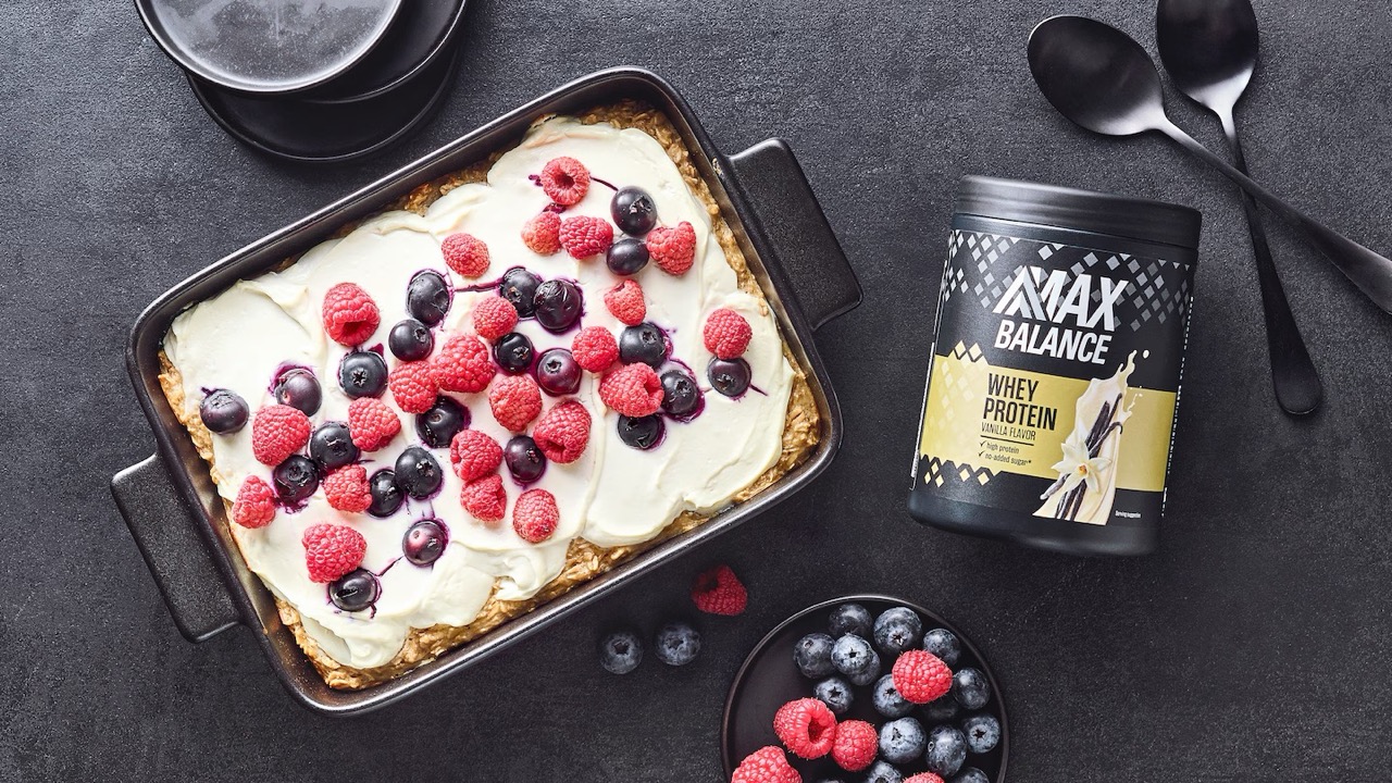 Eine Auflaufform mit Kuchen, weißem Frosting und Beeren. Daneben eine Dose Whey Protein von Max Balance.