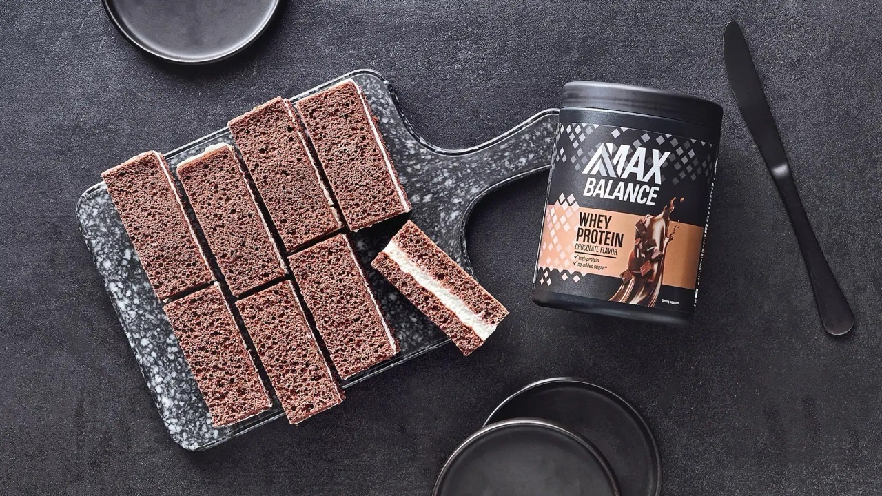 Braune Skyr-Schnitten mit weißer Füllung. Daneben eine Dose Max Balance Whey Protein.
