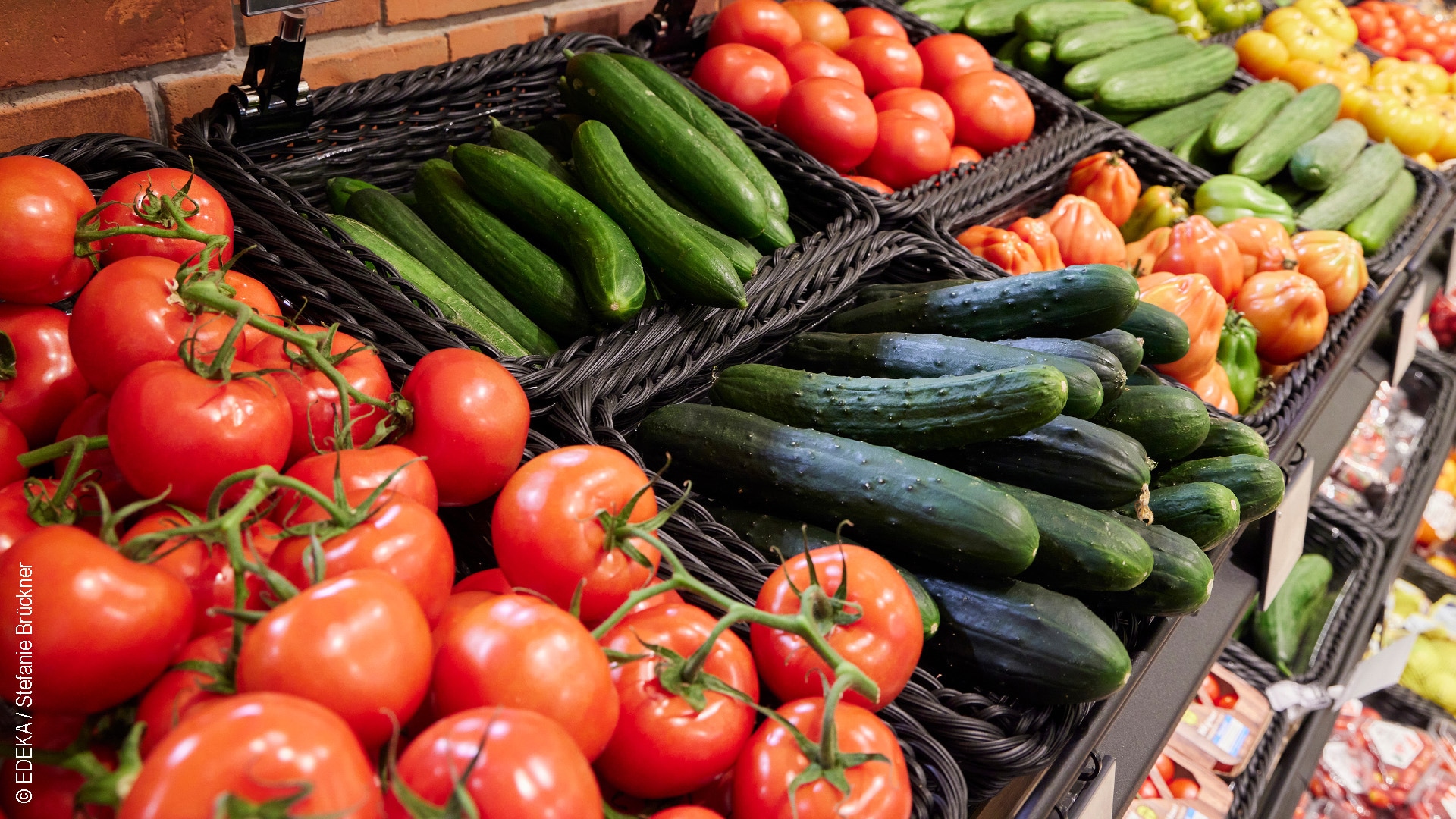 Mehrere schwarze Körbe gefüllt mit verschiedenen Tomaten und Gurken