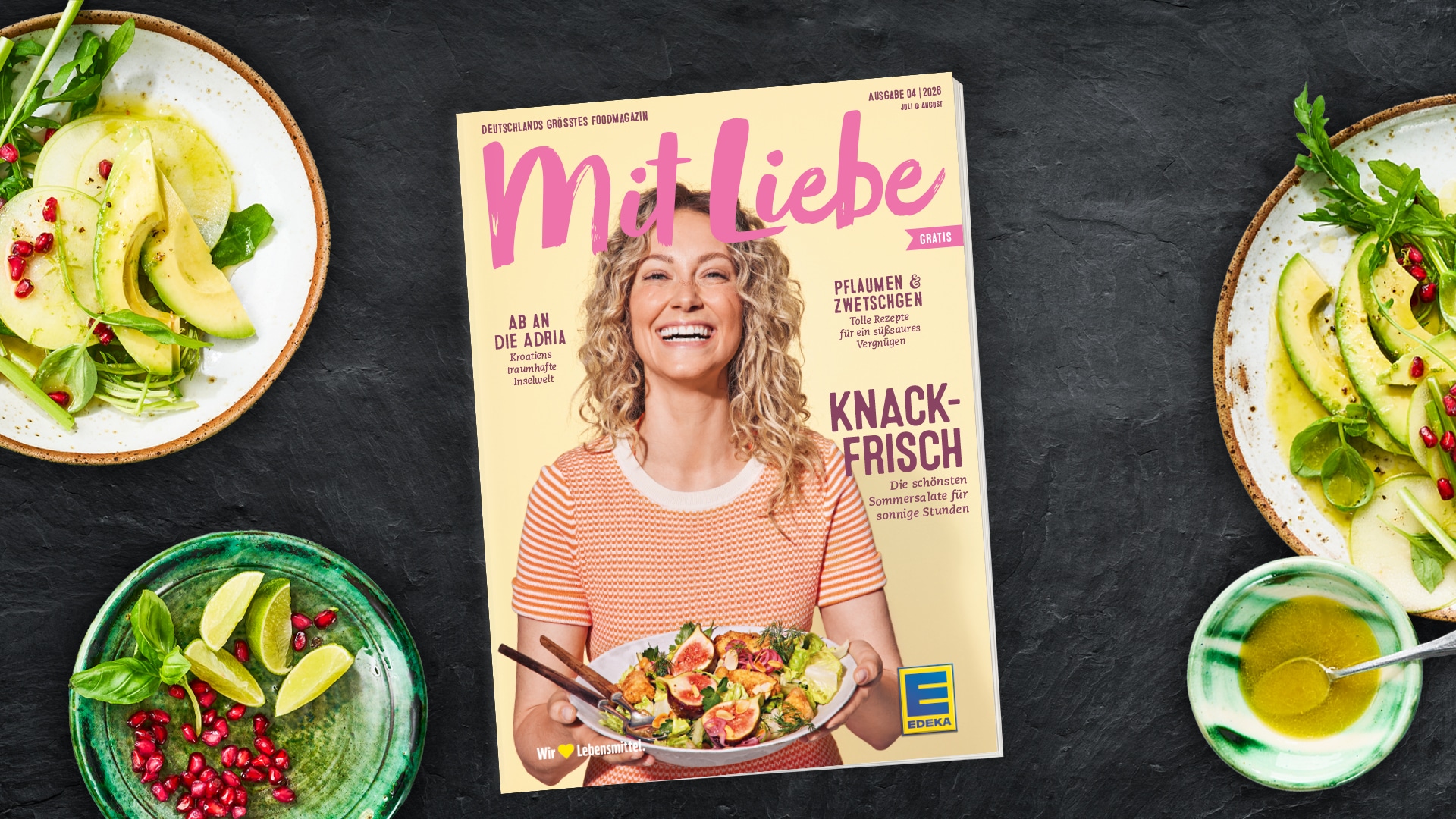Ausgabe des EDEKA-Magazins „Mit Liebe“ auf dunklem Hintergrund, umgeben von Zutaten für Salate wie Avocado, Blattsalat, Limetten und Granatapfelkernen.