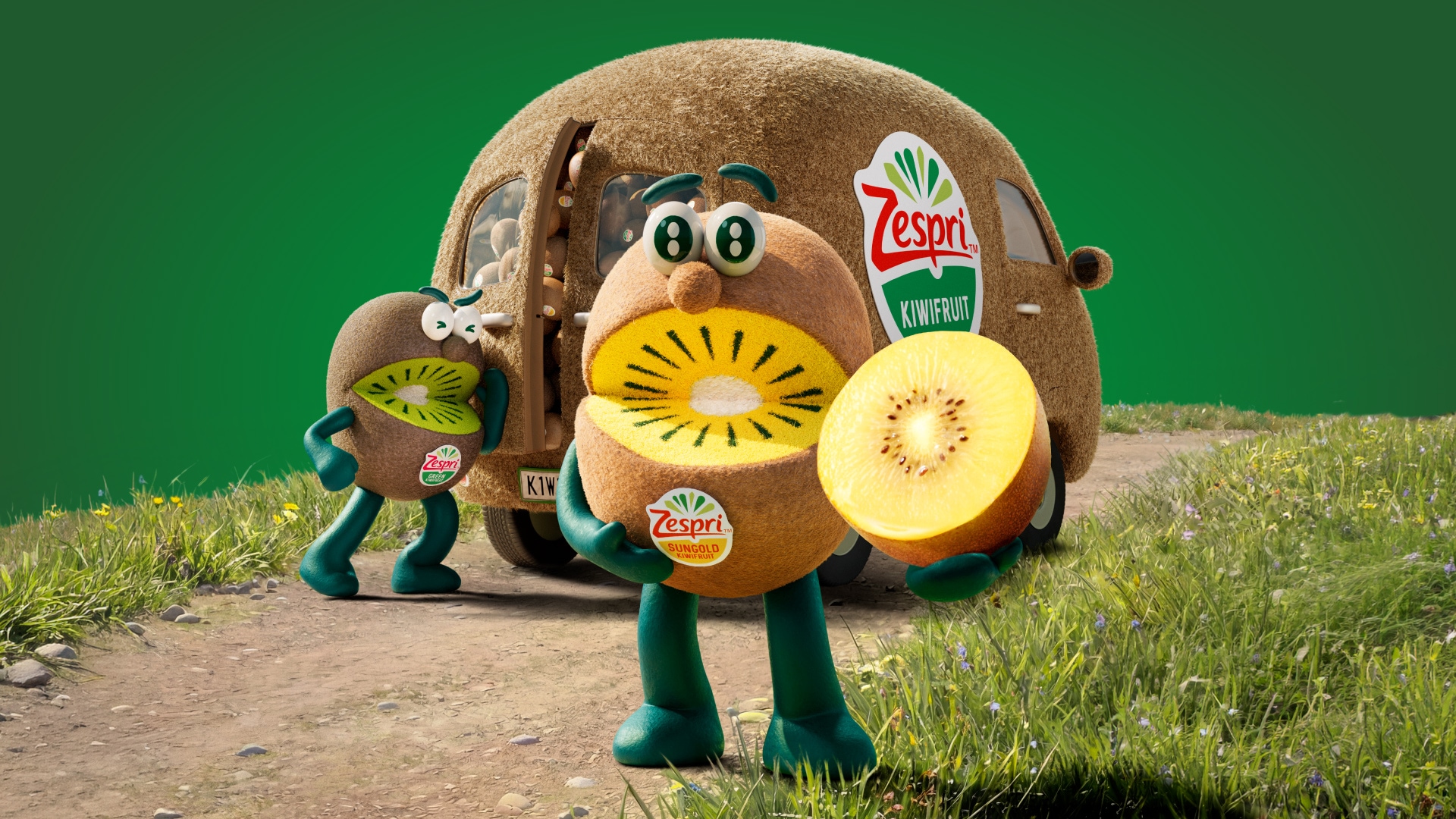 Figur in Form einer Kiwi hält eine aufgeschnittene Goldkiwi (Zespri) vor einem kiwiförmigen Fahrzeug auf einem Feldweg.