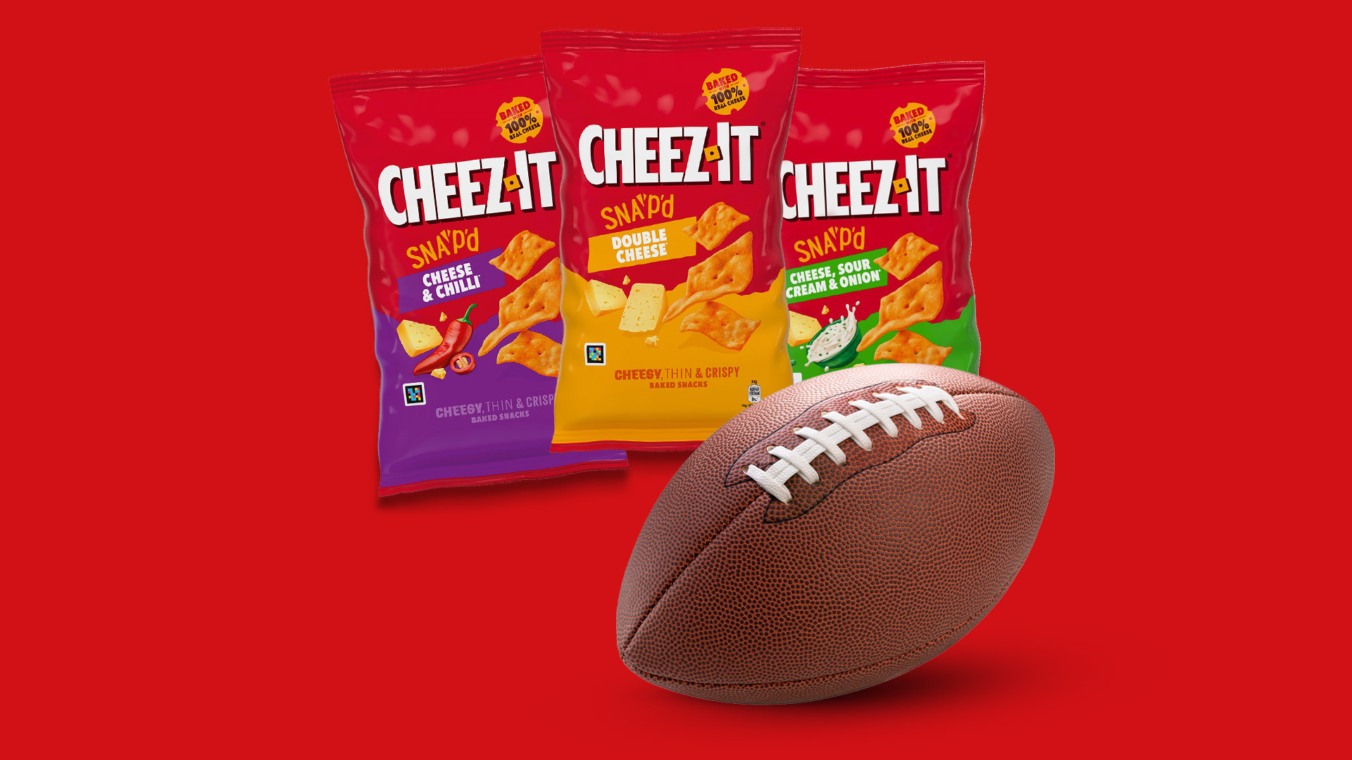 Drei Cheez-It-Snackpackungen in den Sorten Double Cheese, Cheese & Chilli sowie Cheese, Sour Cream & Onion vor rotem Hintergrund, daneben ein Football.