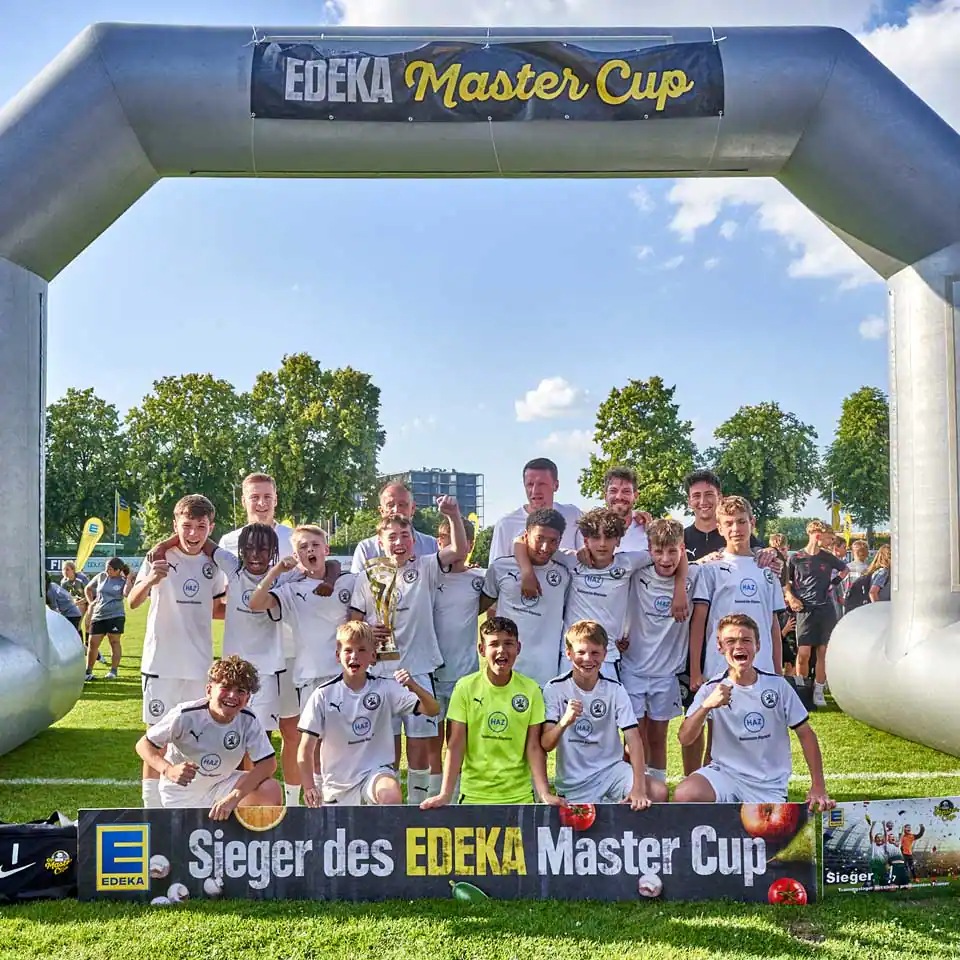Jugendfußballteam posiert jubelnd mit Pokal.