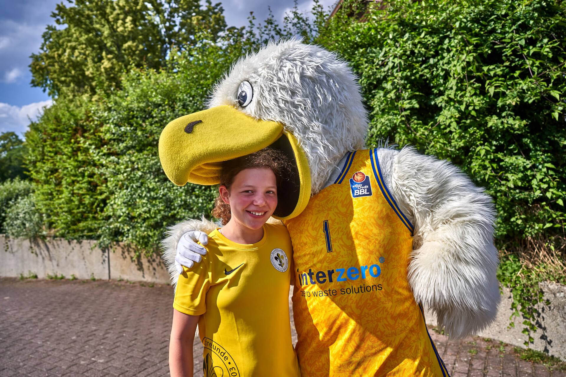 Der Kopf einer Jugend-Fußball-Spielerin steckt im Schnabel des Albatros-Maskottchens.