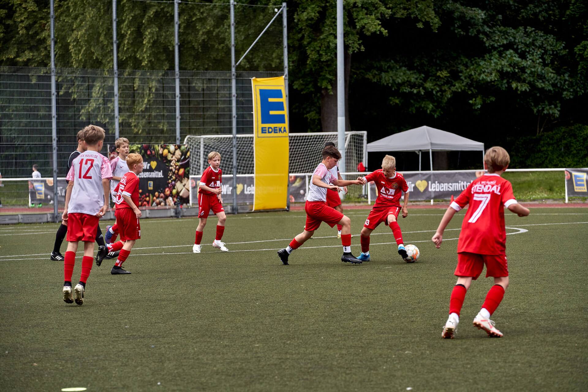 Zwei Jugend-Fußballspieler kämpfen um den Ball. Sie tragen weiße und rote Trikots.