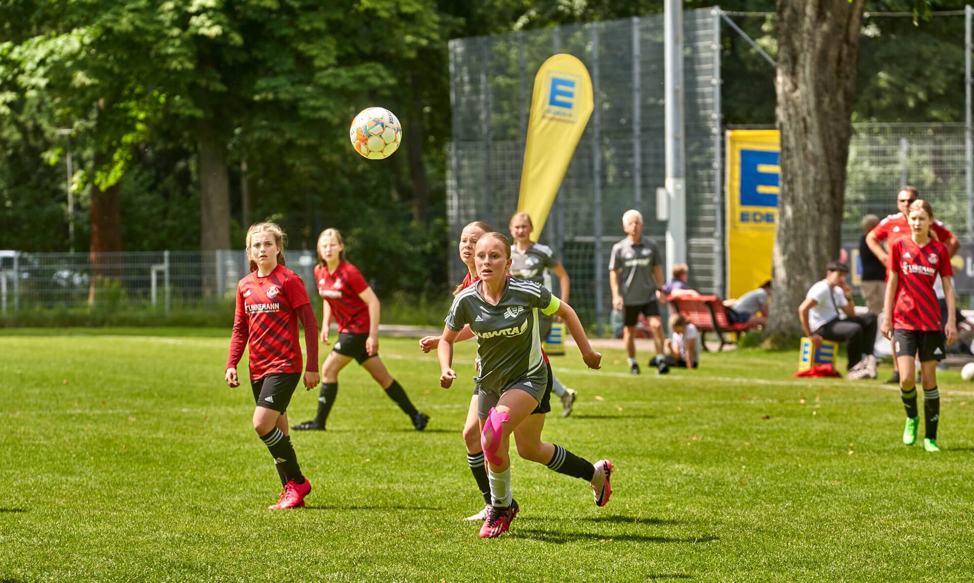 Eine Jugend-Fußballspielerin in grünem Trikot läuft einem hohen Ball hinterher.