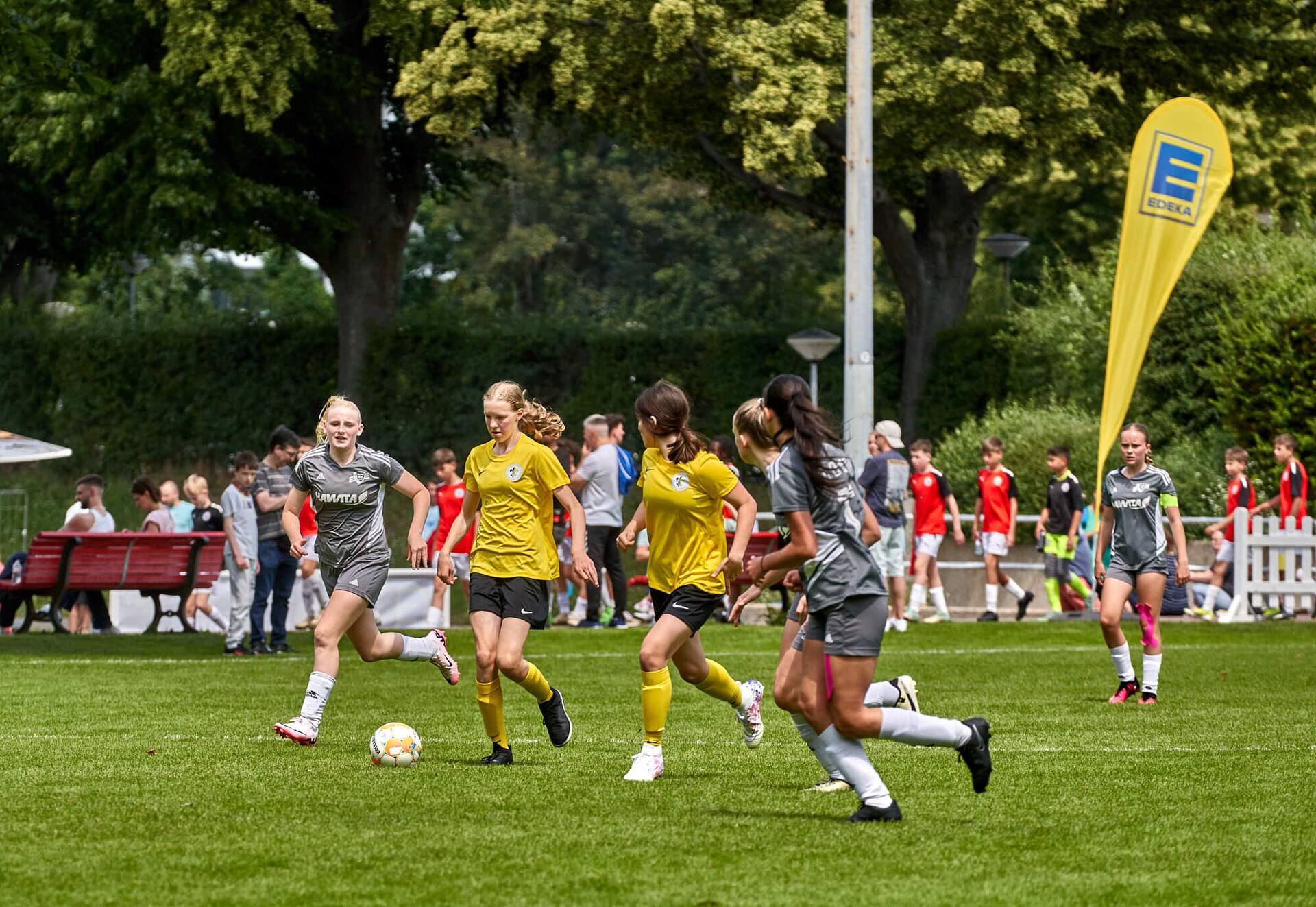 Zwei Jugend-Fußball-Spielerinnen in gelben Trikots versuchen sich gegen drei Gegnerinnen in grauen Trikots durchzusetzen.