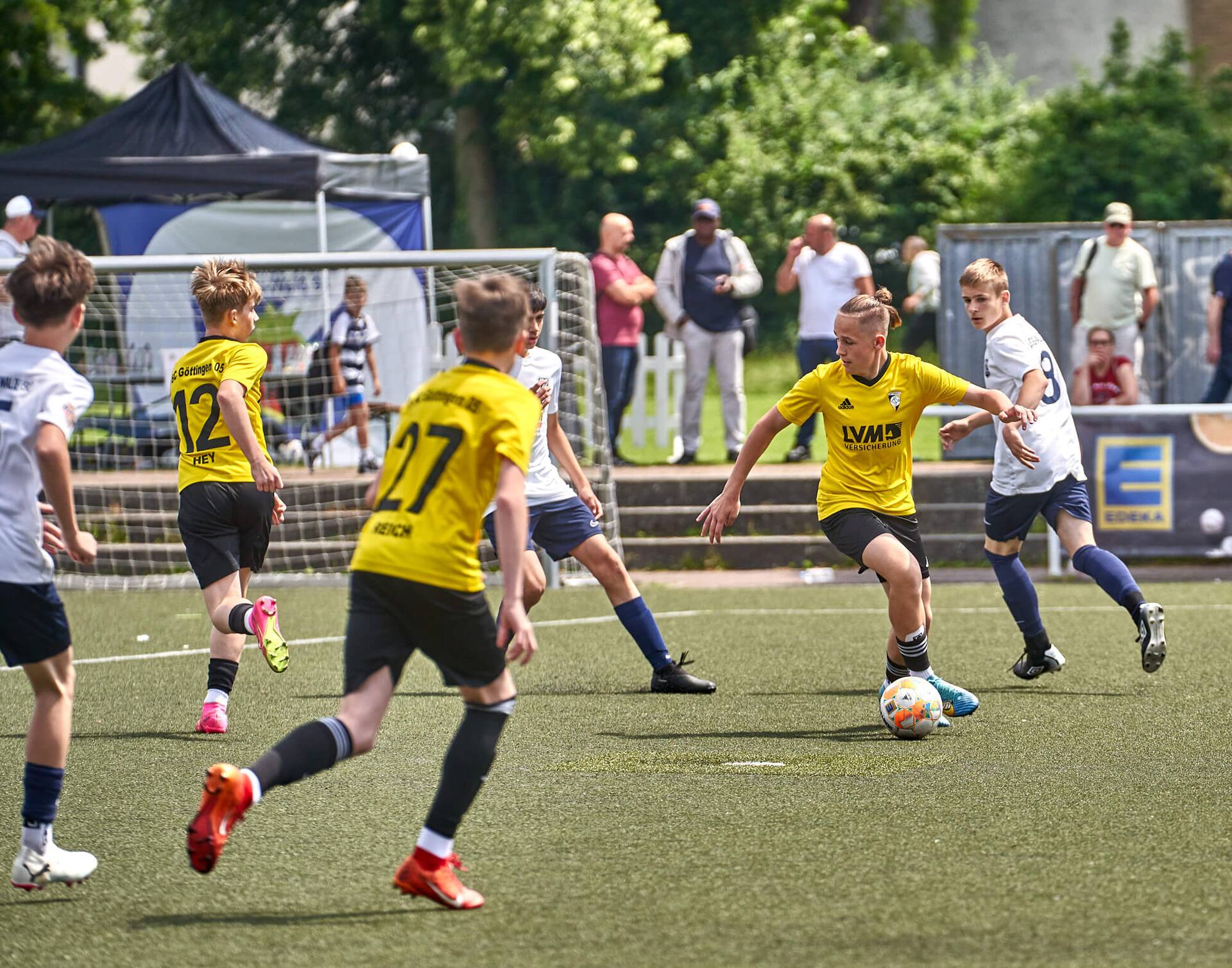 Ein Jugendfußballspieler bewegt sich mit dem Rücken zum Tor, aufrechtem Blick und dem Ball eng am Fuß.