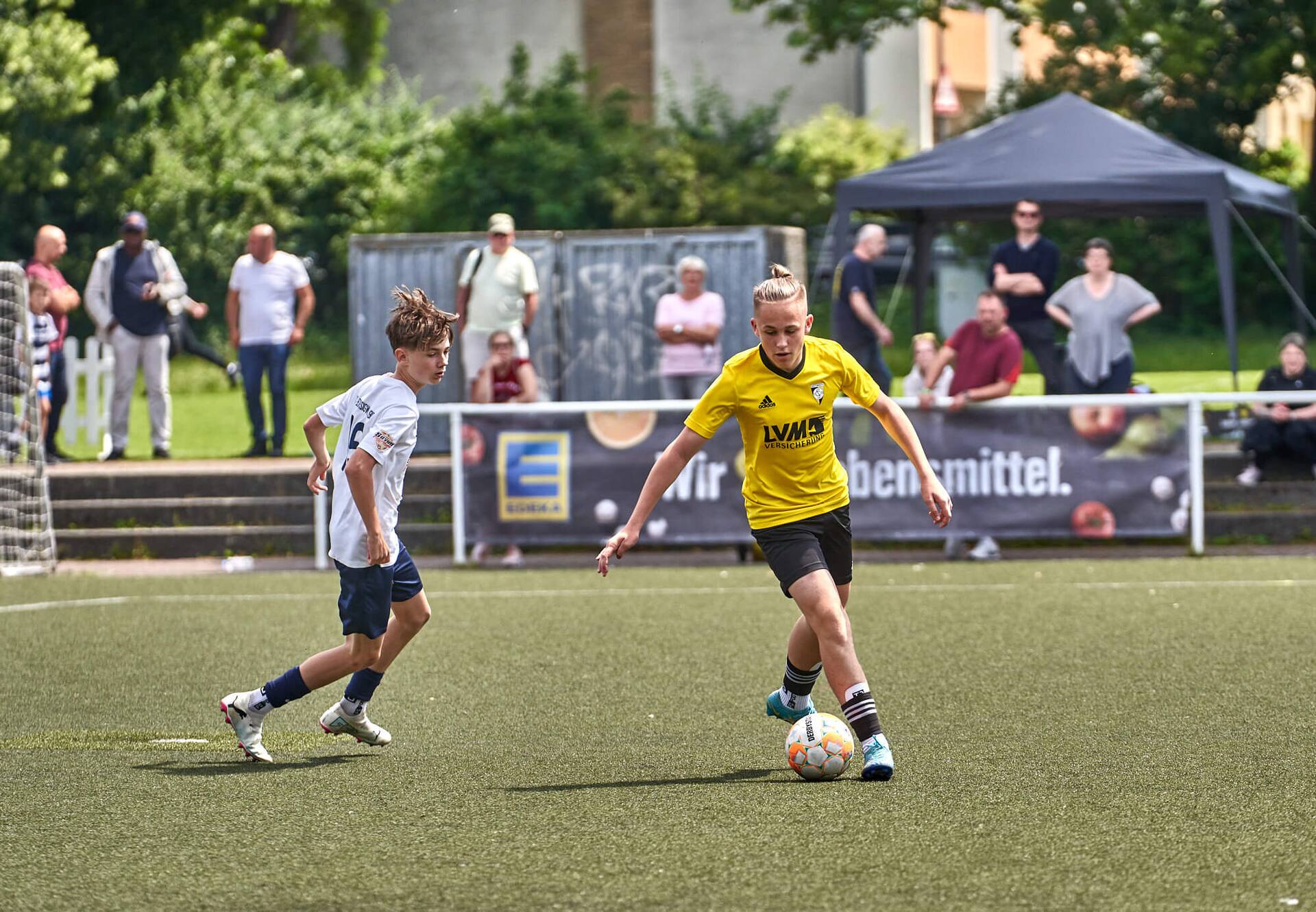Ein Jugendfußballspieler dribbelt mit dem Ball eng am Fuß. Ein Gegenspieler verfolgt ihn.