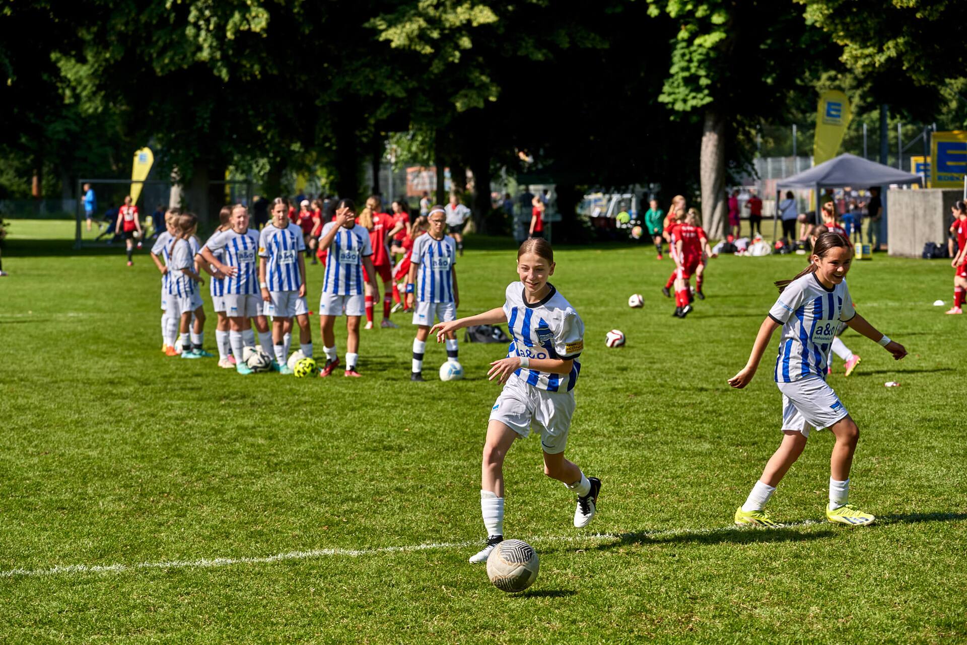 Schussübungen zum Aufwärmen bei einem weiblichen Jugend-Fußballteam in blau-weiß gestreiften Trikots.
