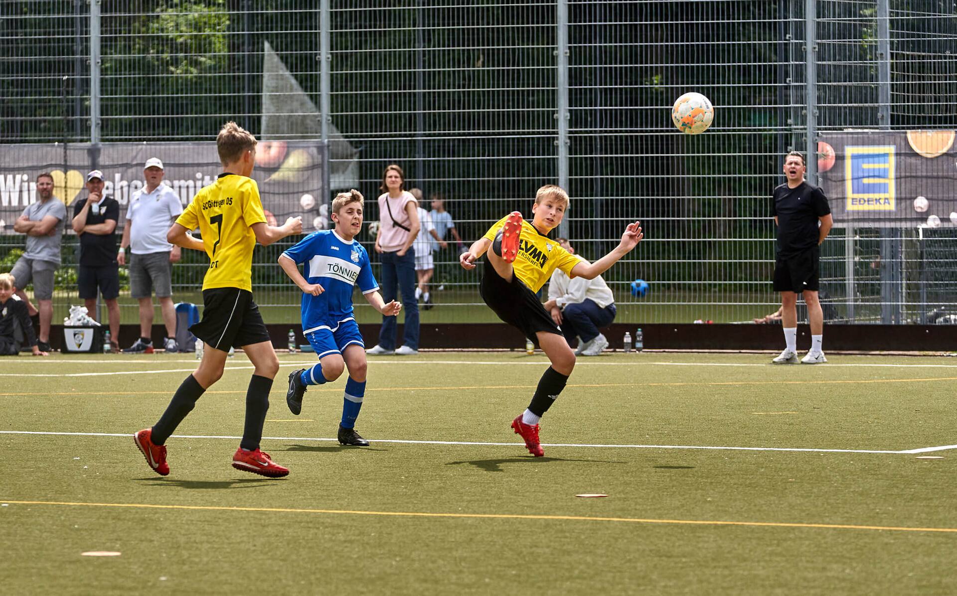 Ein Jugend-Fußballspieler in gelbem Trikot streckt sein Bein hoch, um an den Ball zu kommen.