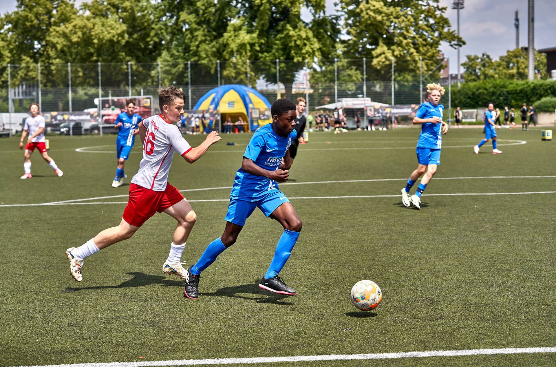 Ein Jugend-Fußballspieler in blau läuft mit dem Ball in Richtung Tor. Sein Gegenspieler rennt hinterher.