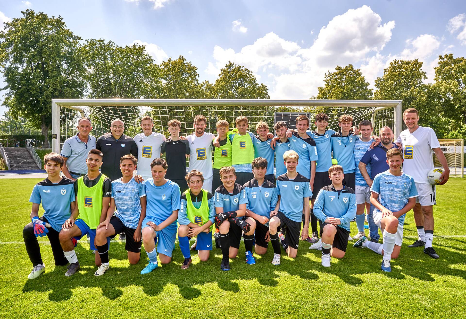 Teambild einer männlichen Fußball-Jugendmannschaft mit Ex-Profis vor einem Tor.