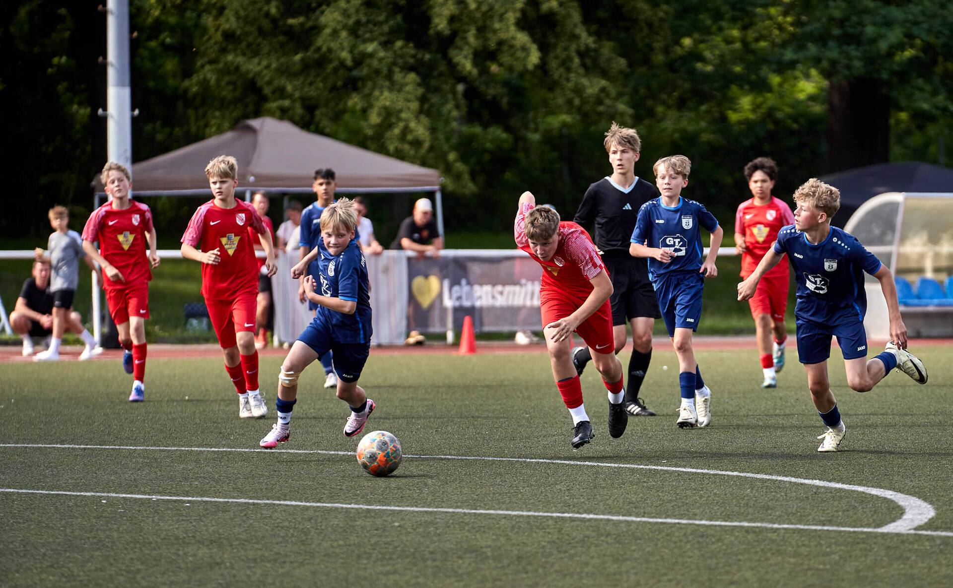 Junge Fußballspieler von zwei Teams rennen dem Ball hinterher.
