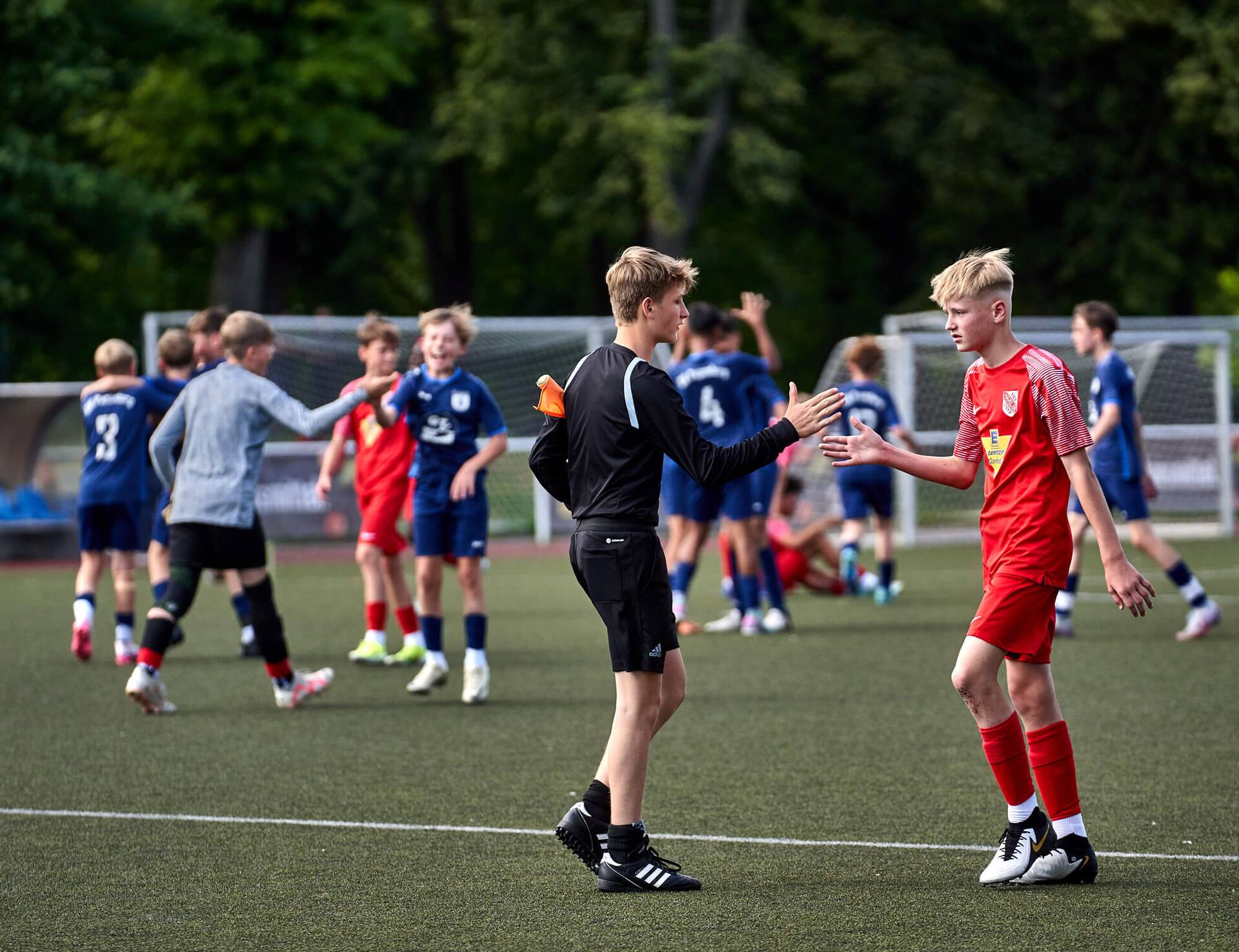 Ein Jugend-Fußballspieler klatscht mit gleichaltrigen Schiedsrichter-Assistenten ab.