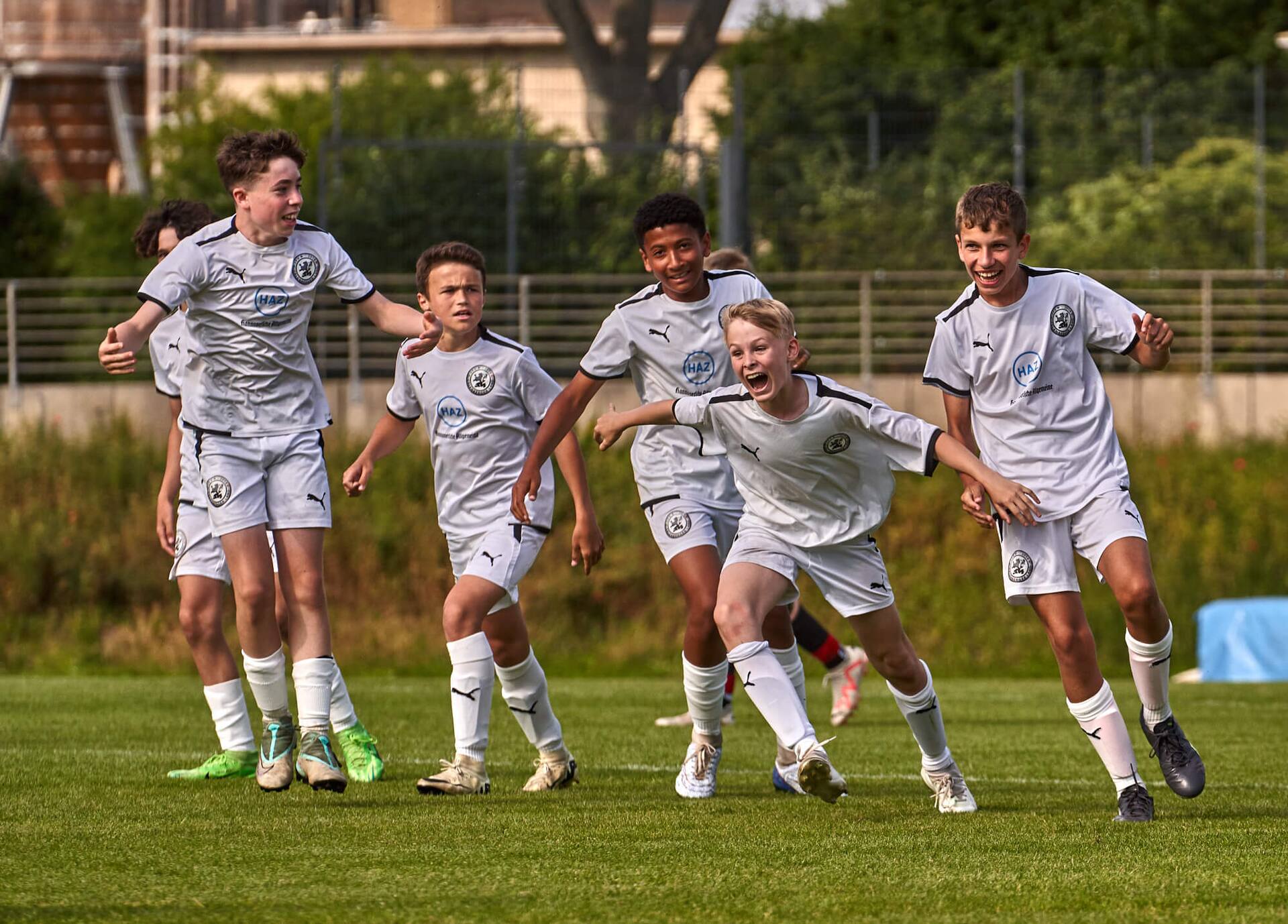 Jubel nach einem Tor bei einem männlichen Jugend-Fußballteam in weißer Spielkleidung.
