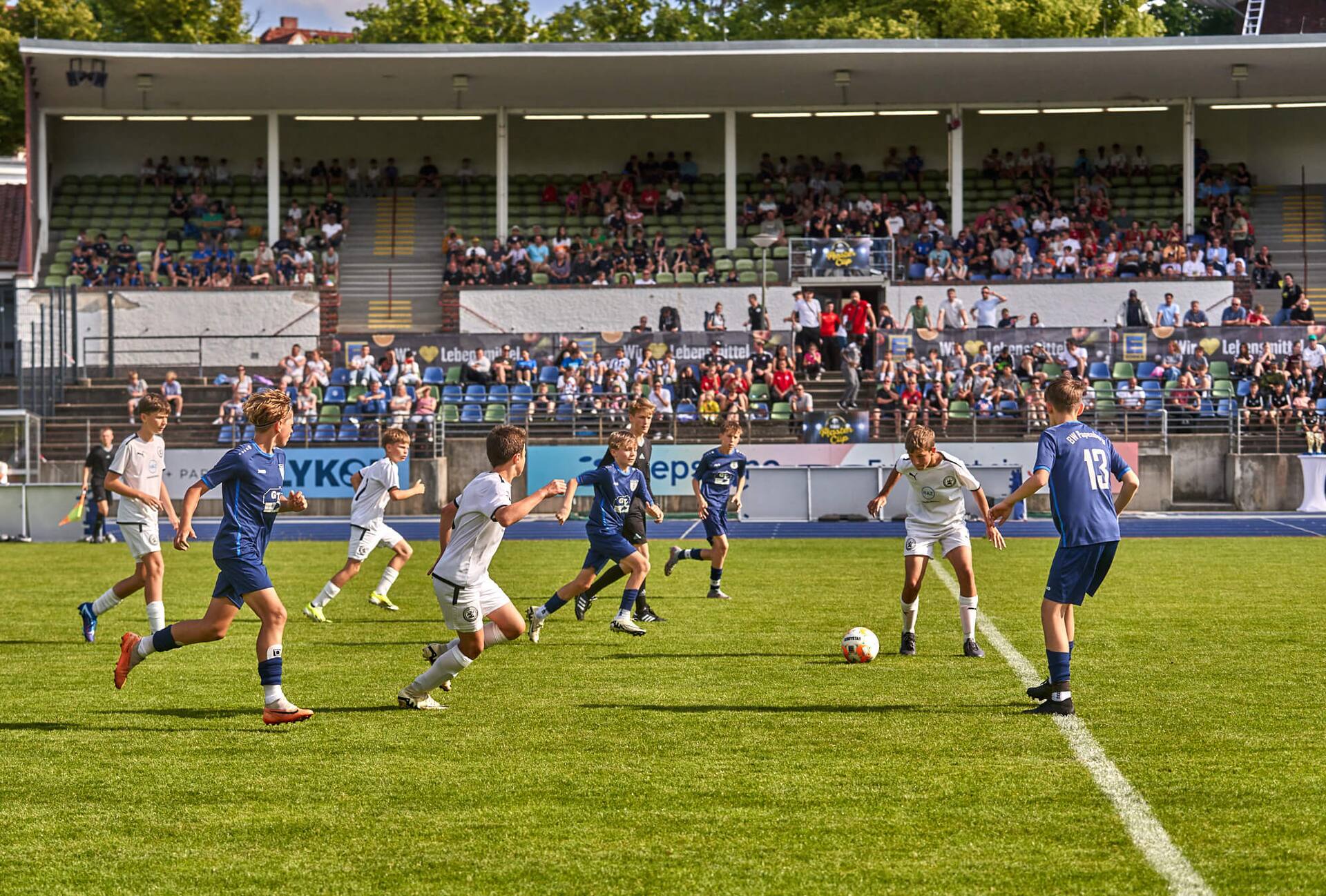 Spielertraube an der Mittellinie. Ein Spieler im weißen Trikot bekommt den Ball.