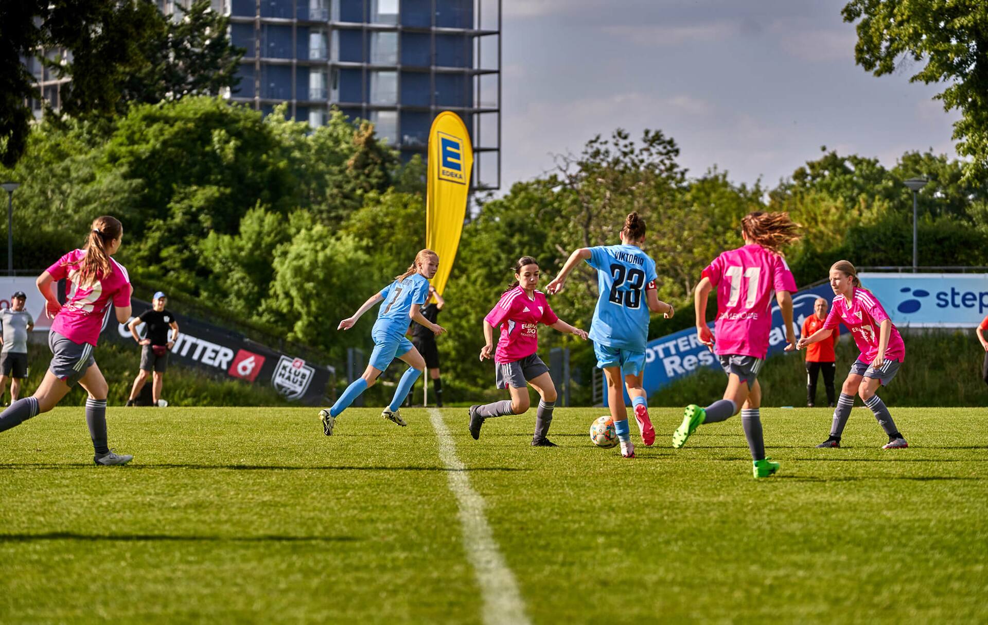 Zweikämpfe im Mittelfeld zwischen einem weiblichen Jugend-Fußballteam in hellblau und einem in hellem Rot.