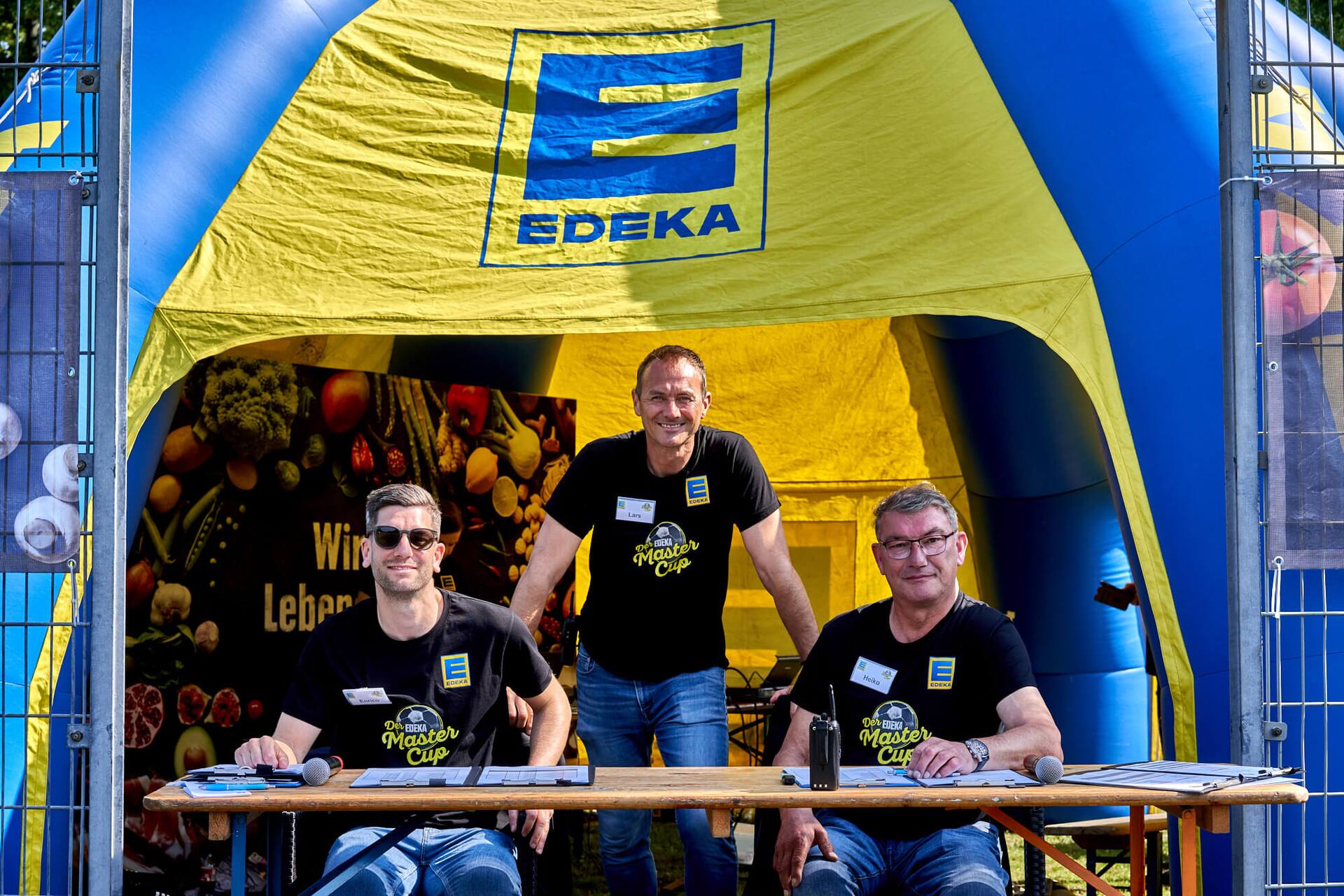 Zwei Männer der Turnierleitung sitzen an einer Bierbank. Ein dritter steht dahinter.