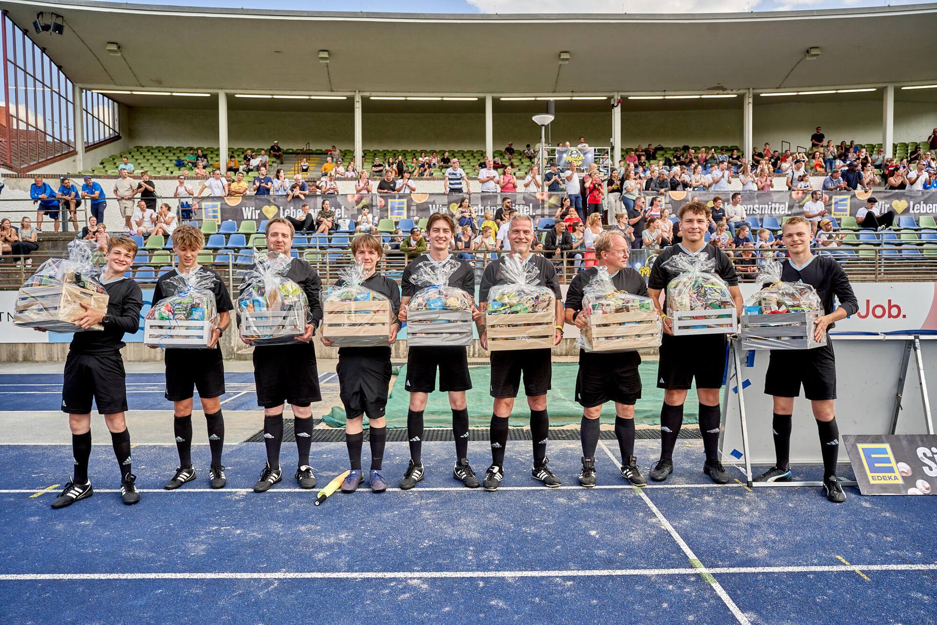 Neun Schiedsrichter mit großen Präsentkörben vor den Zuschauerrängen.