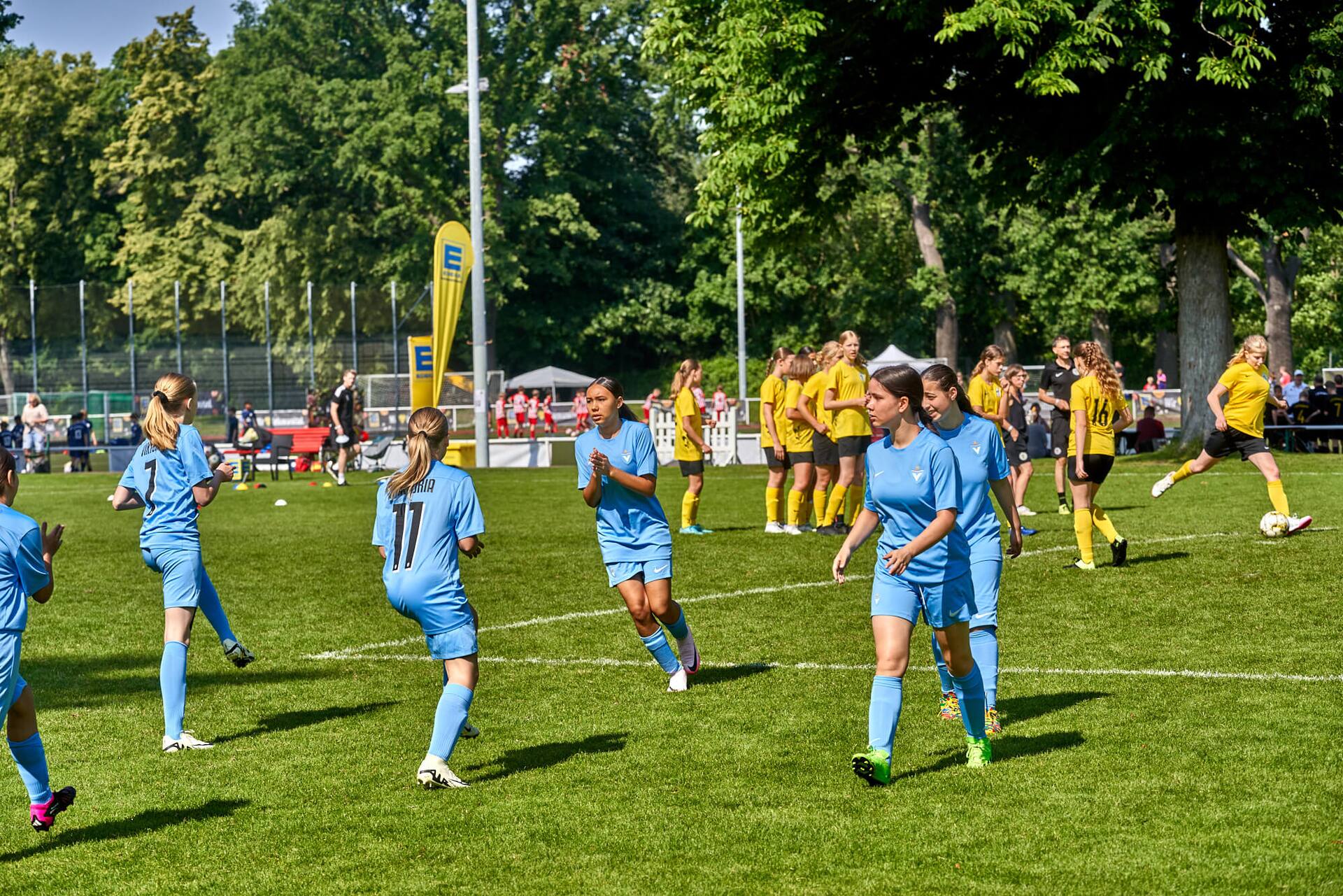 Aufwärmübungen zweier weiblicher Jugend-Fußballteams – eins in blau, eins in gelb.