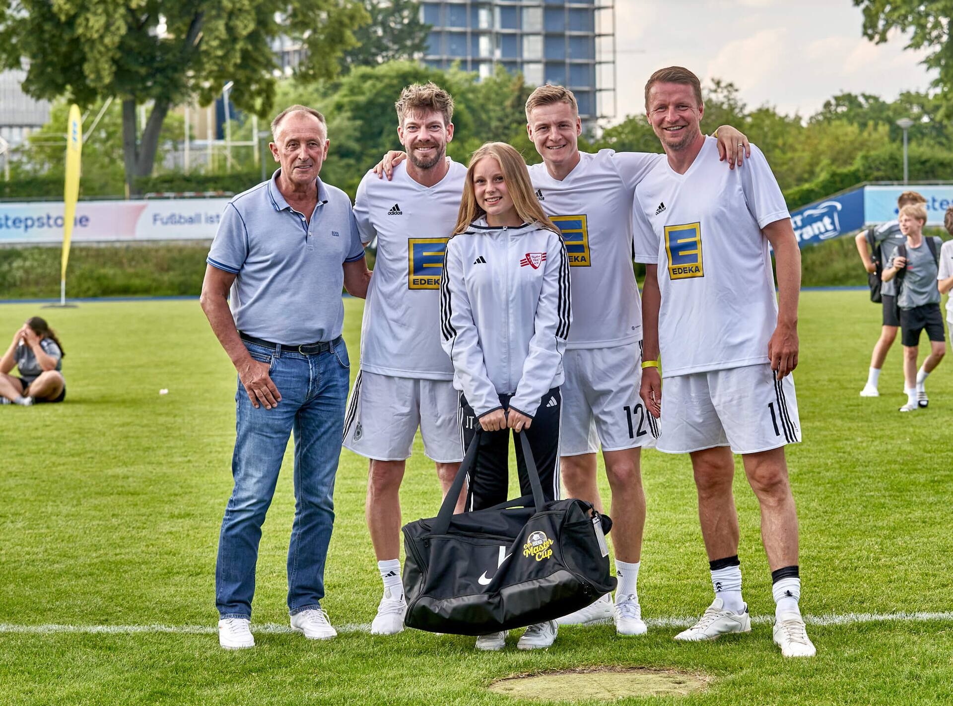 Drei Ex-Profis und ein älterer Herr stehen mit einer Jugendfußballspielerin zusammen. Sie hält eine große neue Sporttasche in der Hand.
