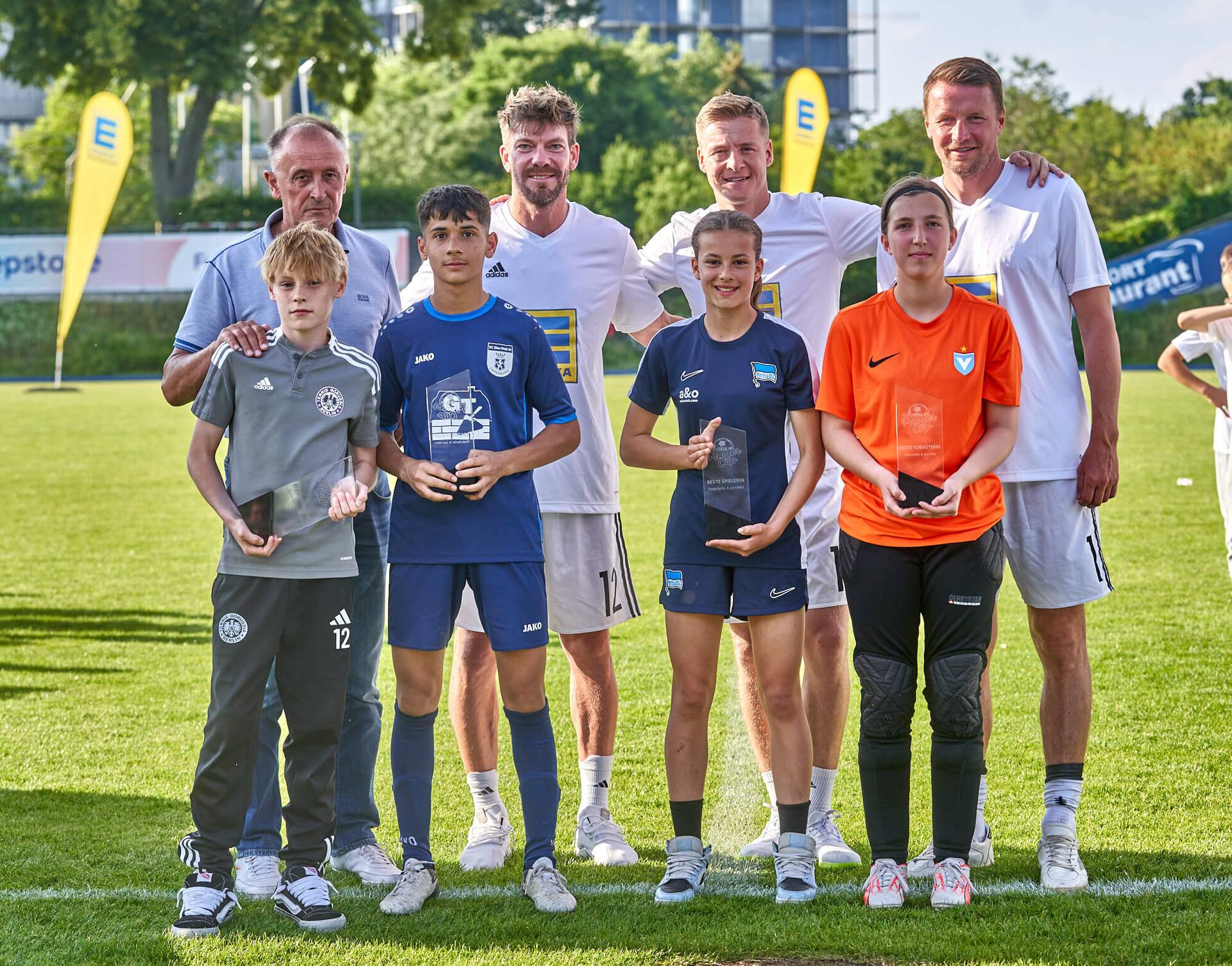 Drei Ex-Profis und ein älterer Herr stehen mit vier prämierten Spielerinnen und Spielern mit Pokalen zusammen.