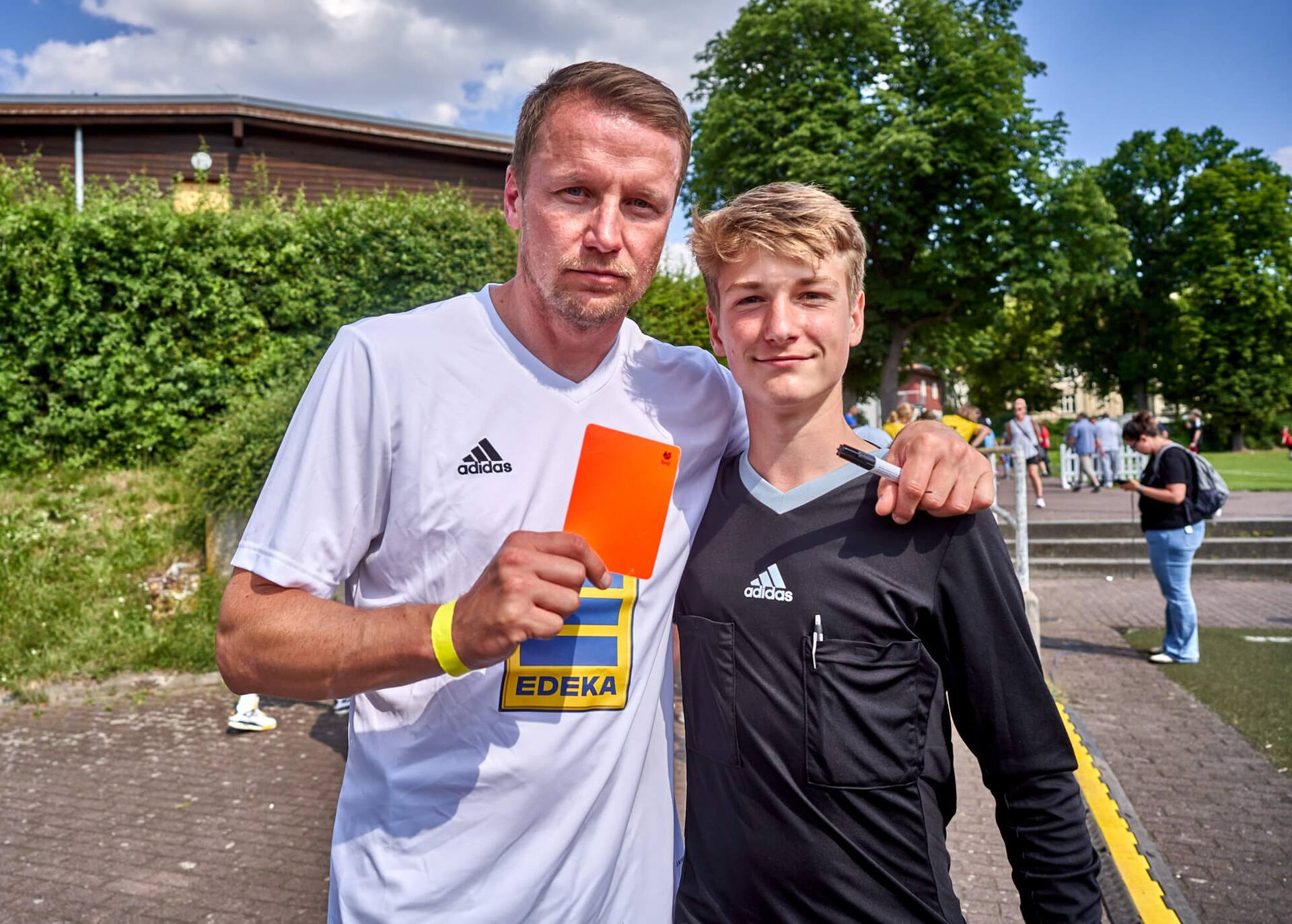 Maik Franz steht neben einem jungen Schiedsrichter. Der Ex-Profi hält eine Rote Karte in der Hand.