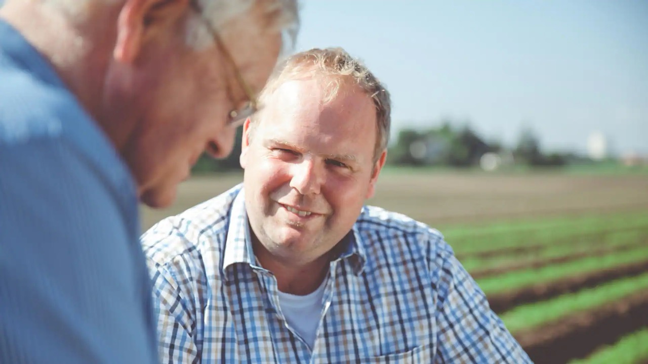 Ein Mann hockt auf einem bestellten Feld und lächelt.